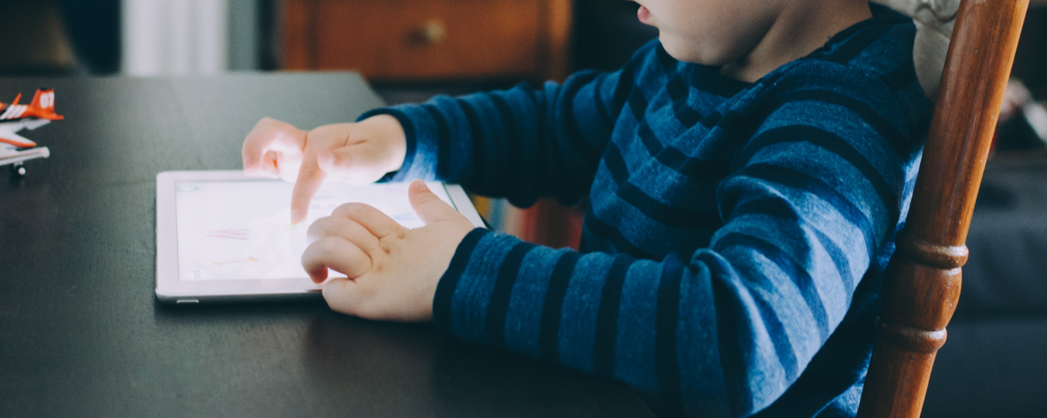 A kid using an iPad on a table.